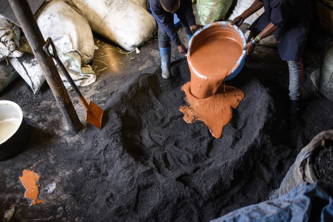 Workers adding a liquid binder to prepared charcoal powder during briquette production